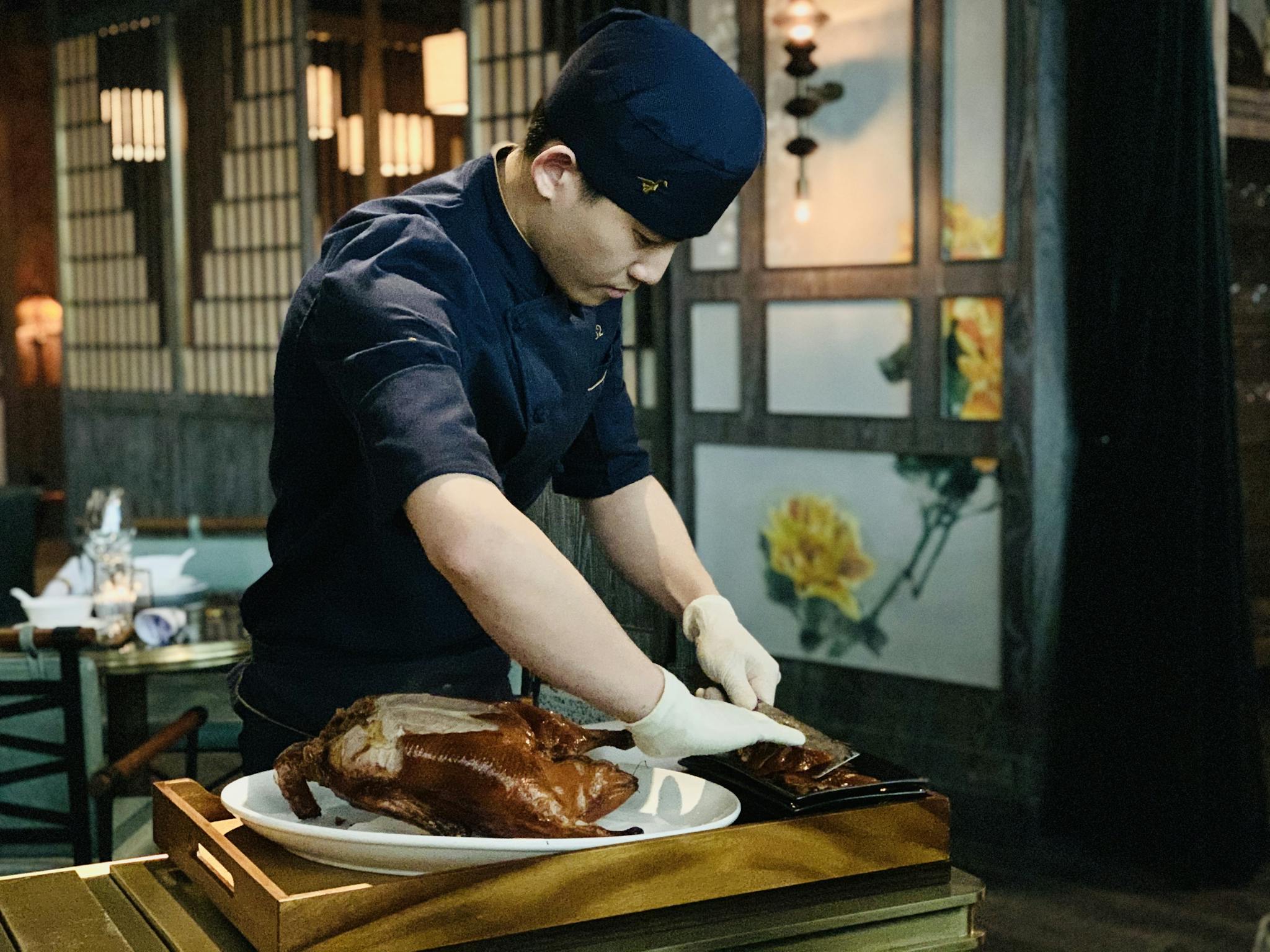 Ethnic male cook cutting roasted duck